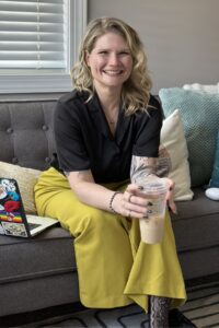 Courtney sitting on a gray couch at Empower Counseling, smiling while holding an iced coffee, with a laptop nearby in the therapy office.